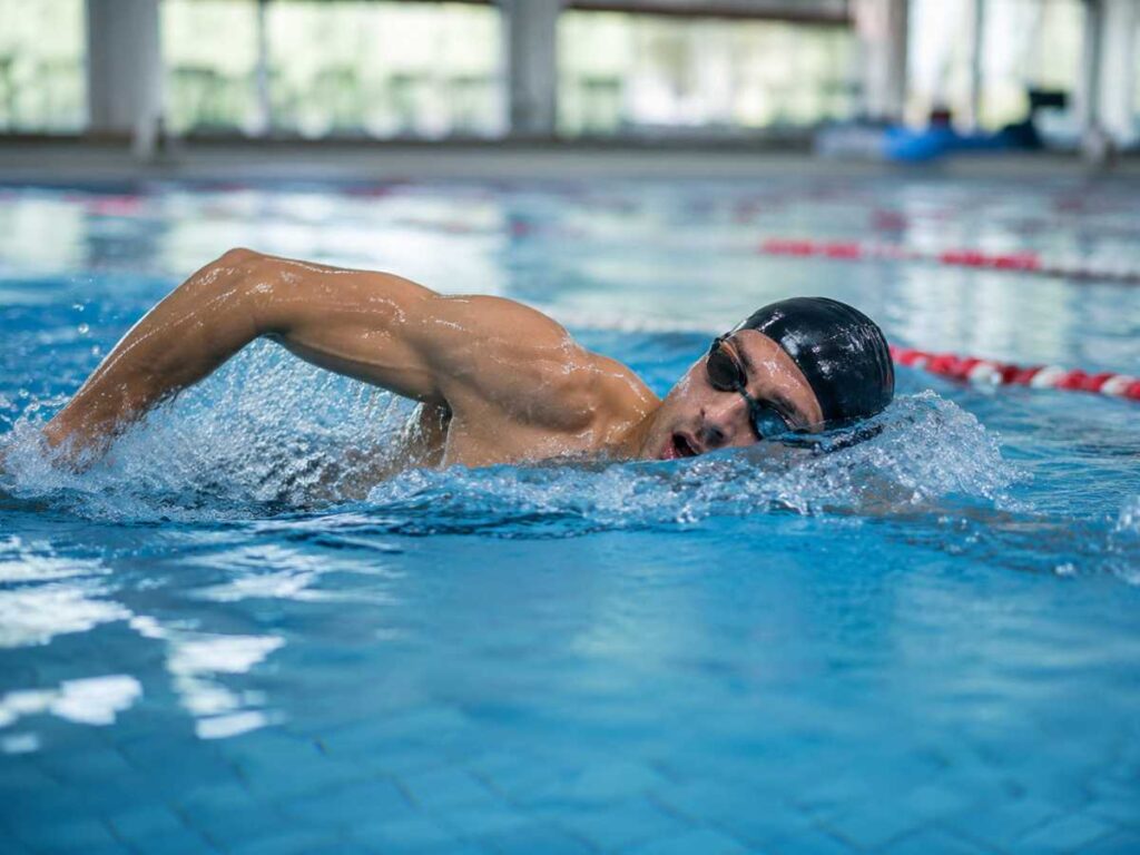 Swimmer doing freestyle laps in a clear blue pool, showing swimming as one of the best endurance exercises for stamina.