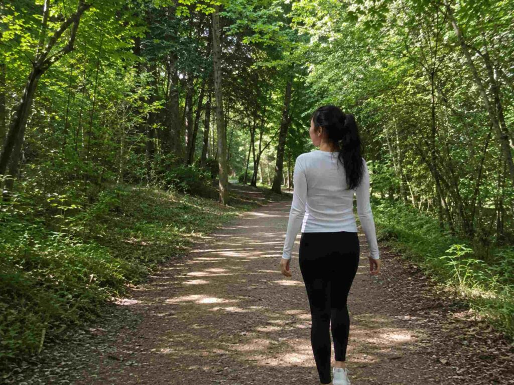 Woman walking briskly on a sunny park trail, showing walking as one of the best endurance exercises for beginners.